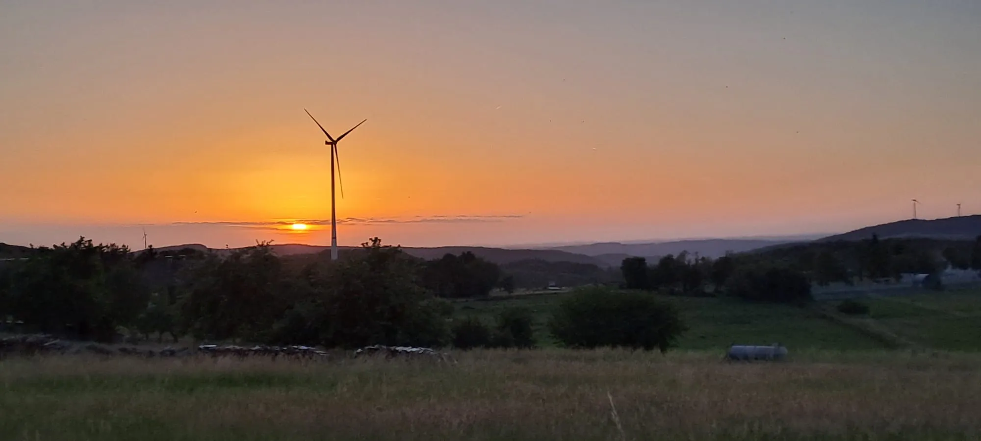 Untergehende Sonne hinter einer Windkraftanlage über den Feldern bei Gielert